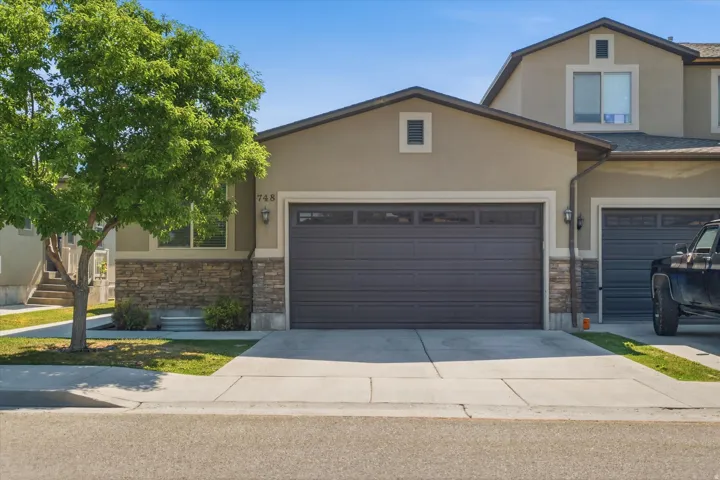 Stucco exterior with stone veneer accents and a two-car garage featuring transom windows
