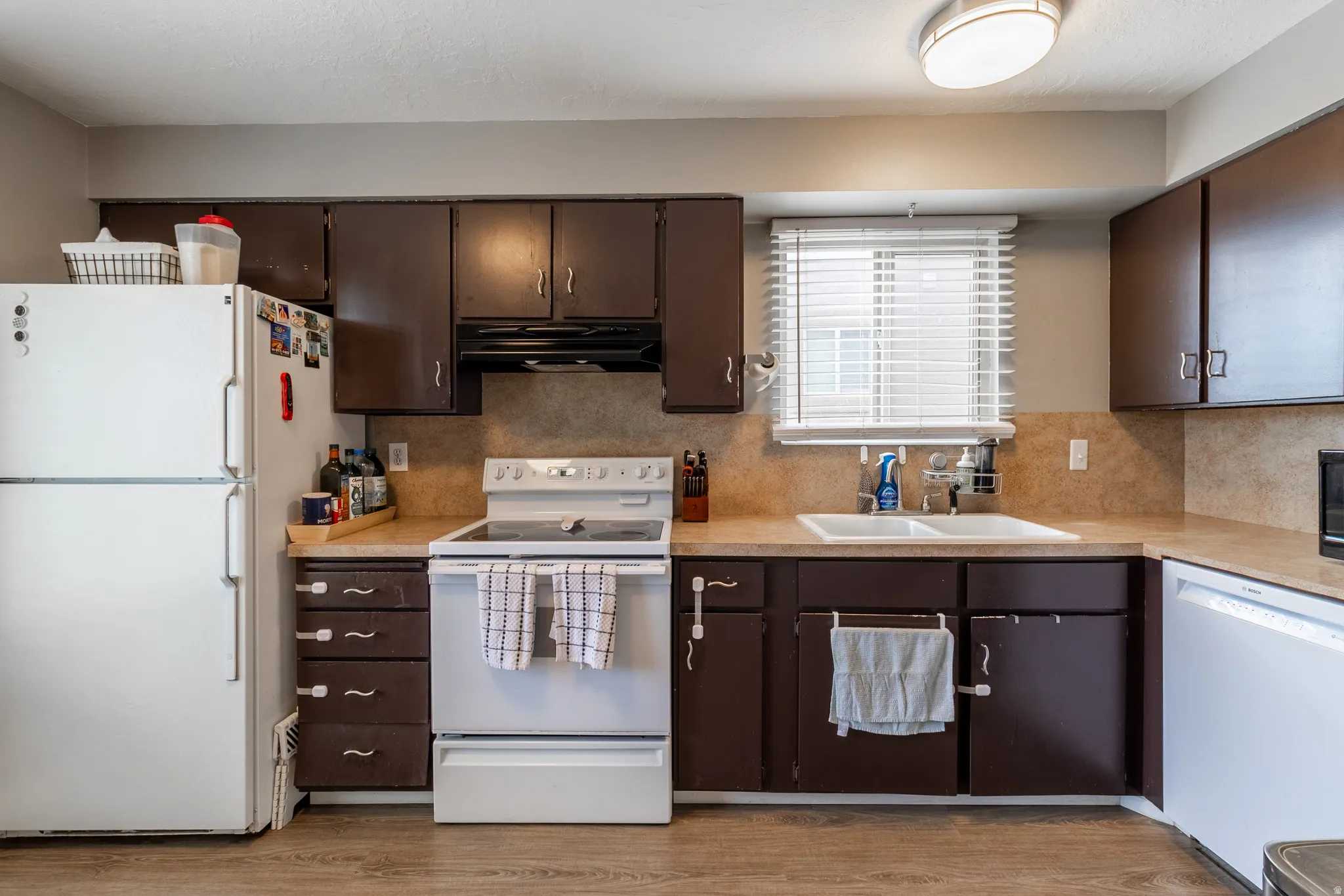 Kitchen featuring wood-finish flooring, dark wood cabinetry, a double basin sink, and a window with blinds