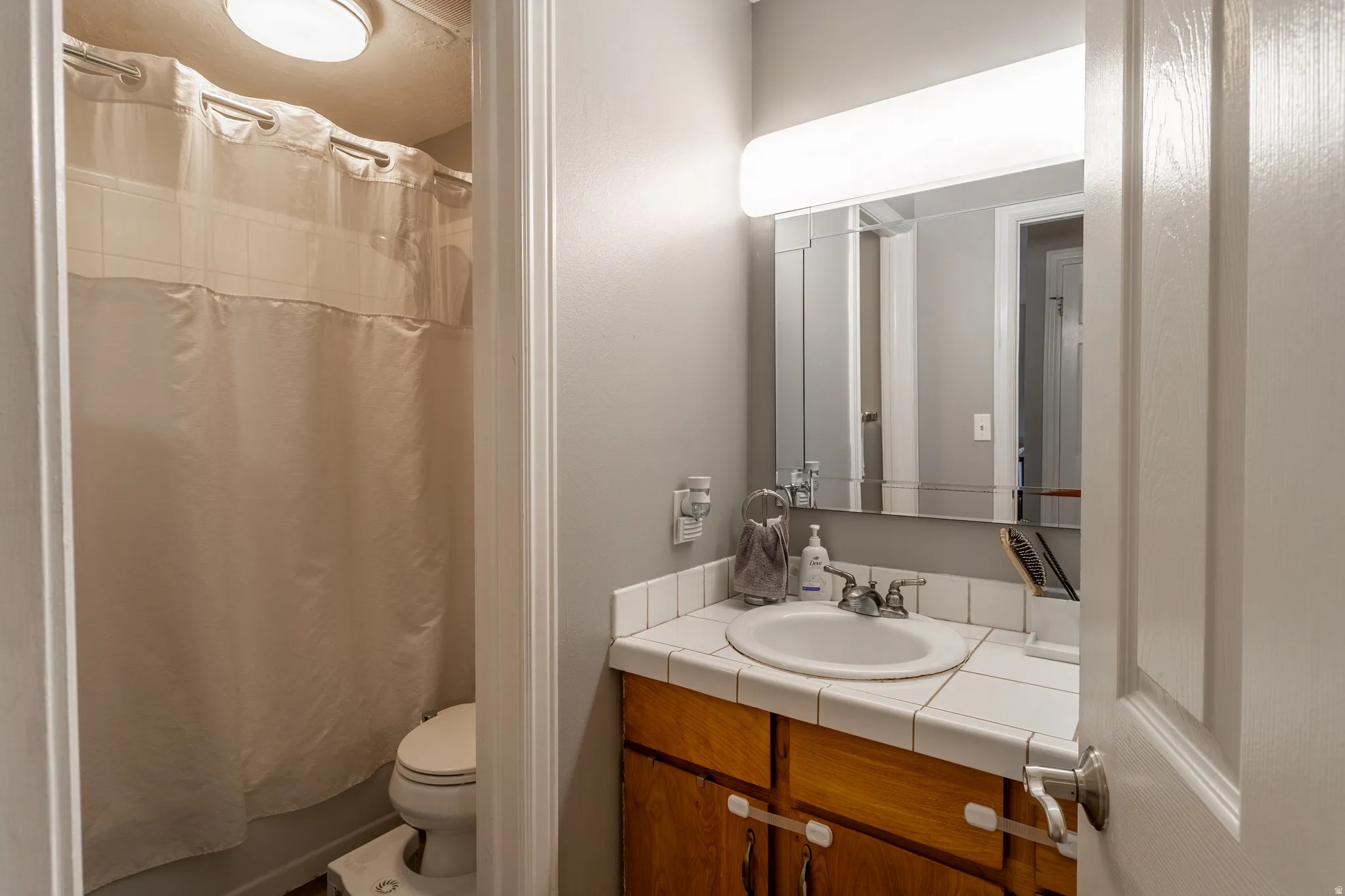 Bathroom with a vanity featuring a drop-in sink, tile countertop, and wood-finish cabinetry