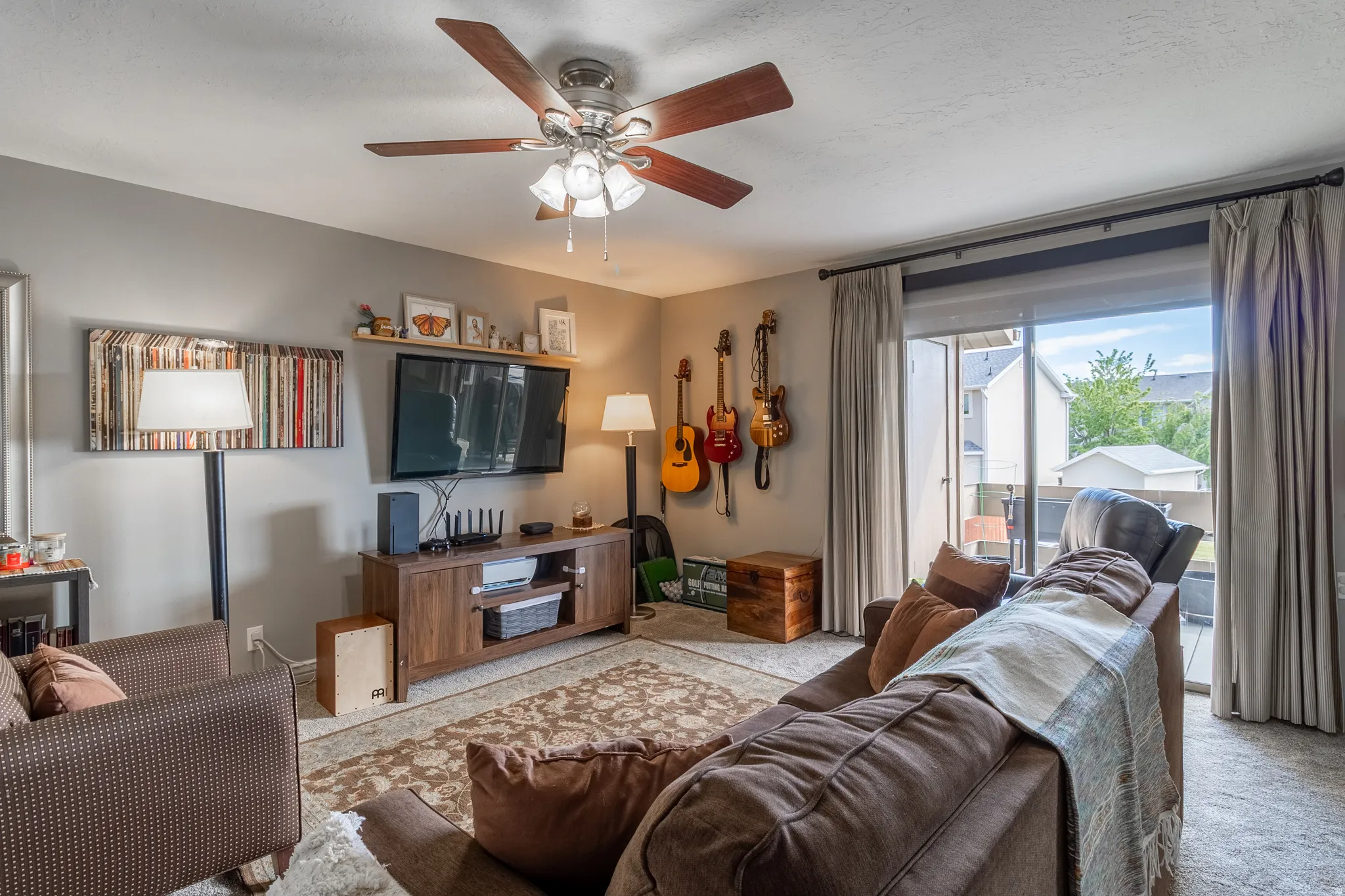 Living area featuring a ceiling fan, sliding glass door, and wall-mounted shelving