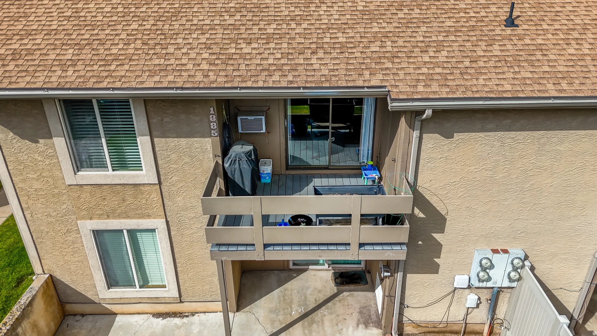 Two-story stucco exterior featuring a private second-level balcony, ground-level patio, multiple windows, and a sliding glass door