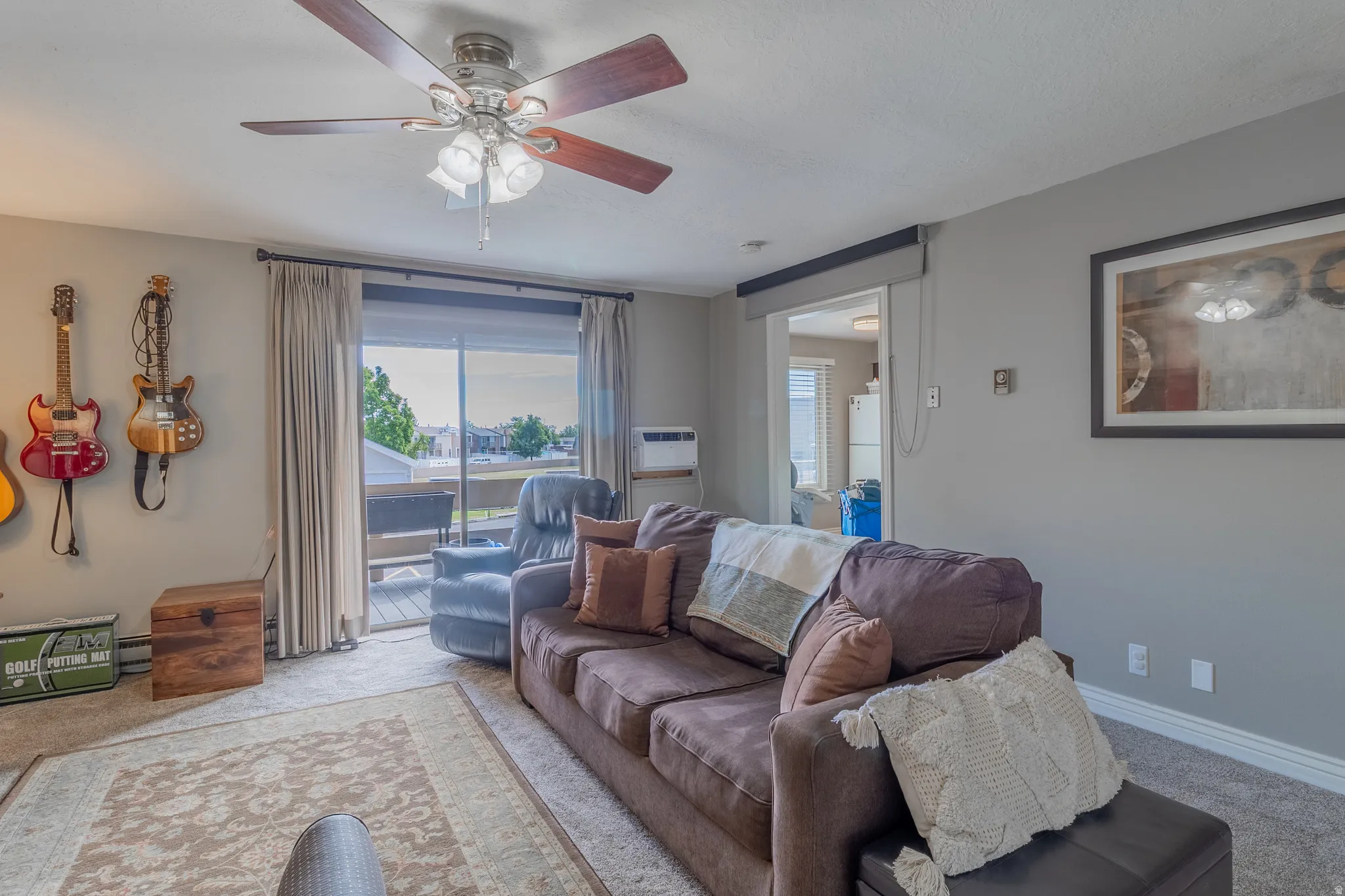 Living area featuring a ceiling fan with integrated lighting, neutral-toned walls, and carpet flooring with an area rug