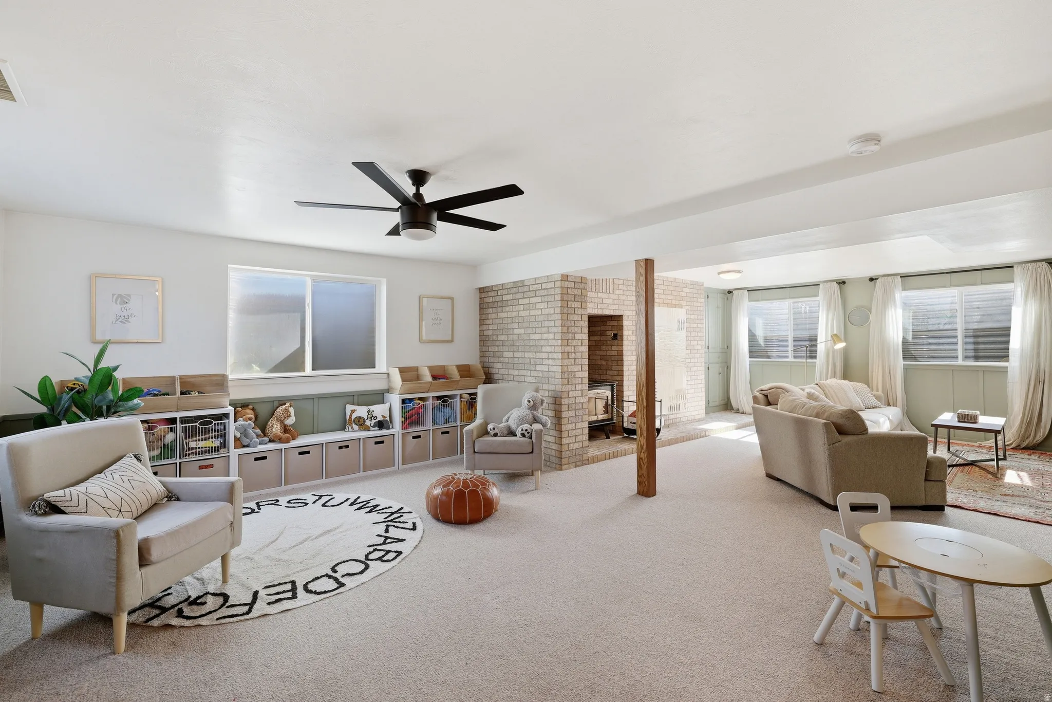 Expansive finished basement with carpet flooring, a ceiling fan, and a brick-surround fireplace
