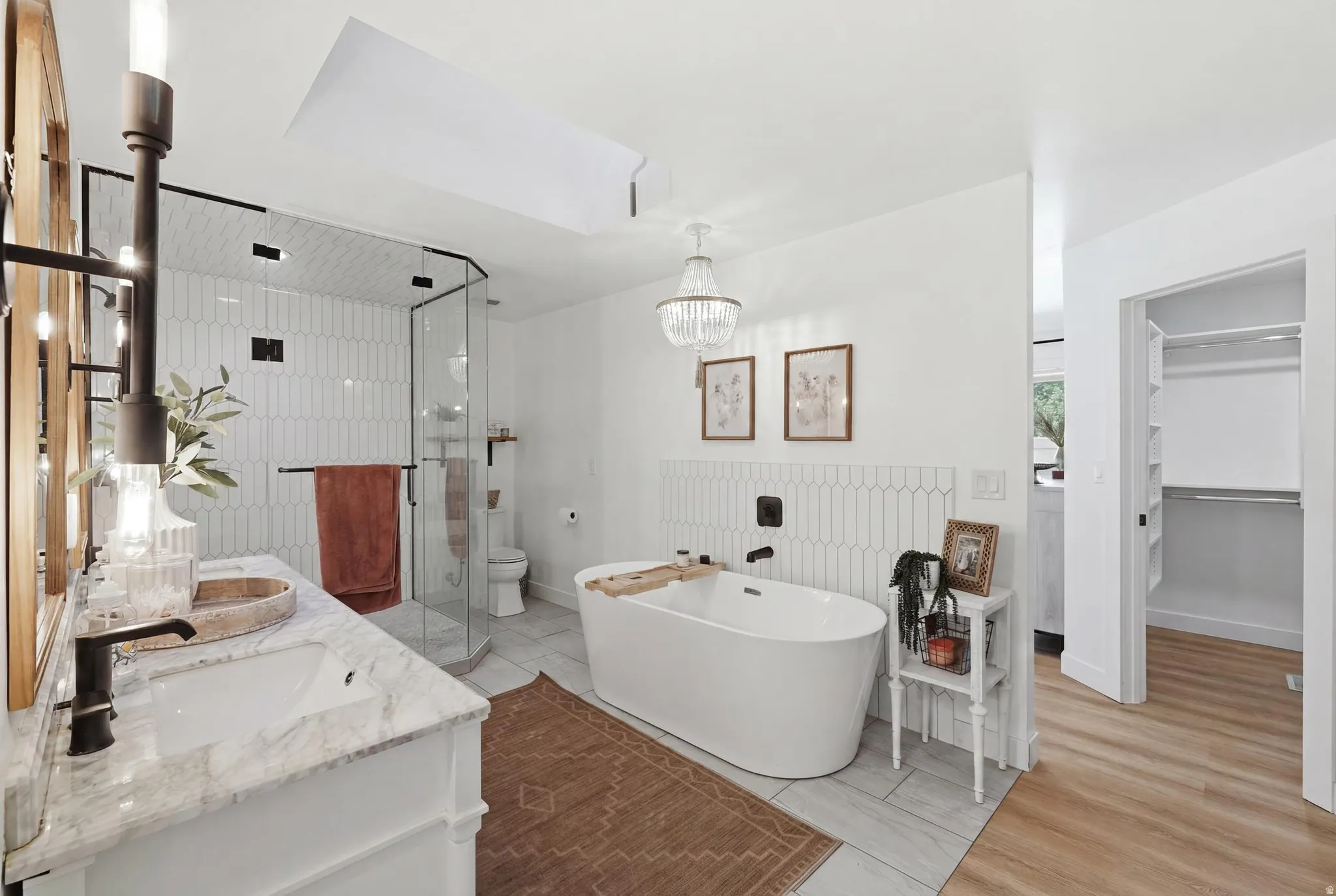 Bathroom featuring a freestanding soaking tub, dual vanity with marble countertops, a skylight, and a glass-enclosed shower with vertical picket tile