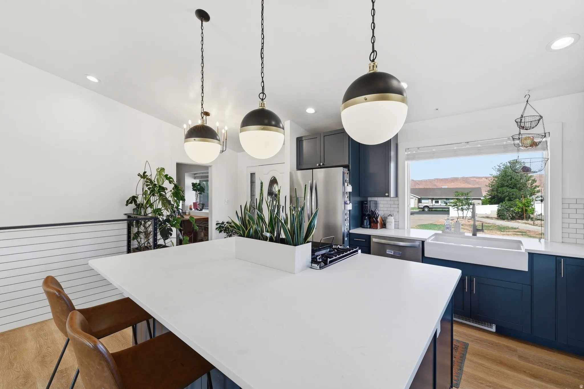 Spacious kitchen featuring a large central island with a white countertop, dark blue cabinetry, white subway tile backsplash, and a white farmhouse sink