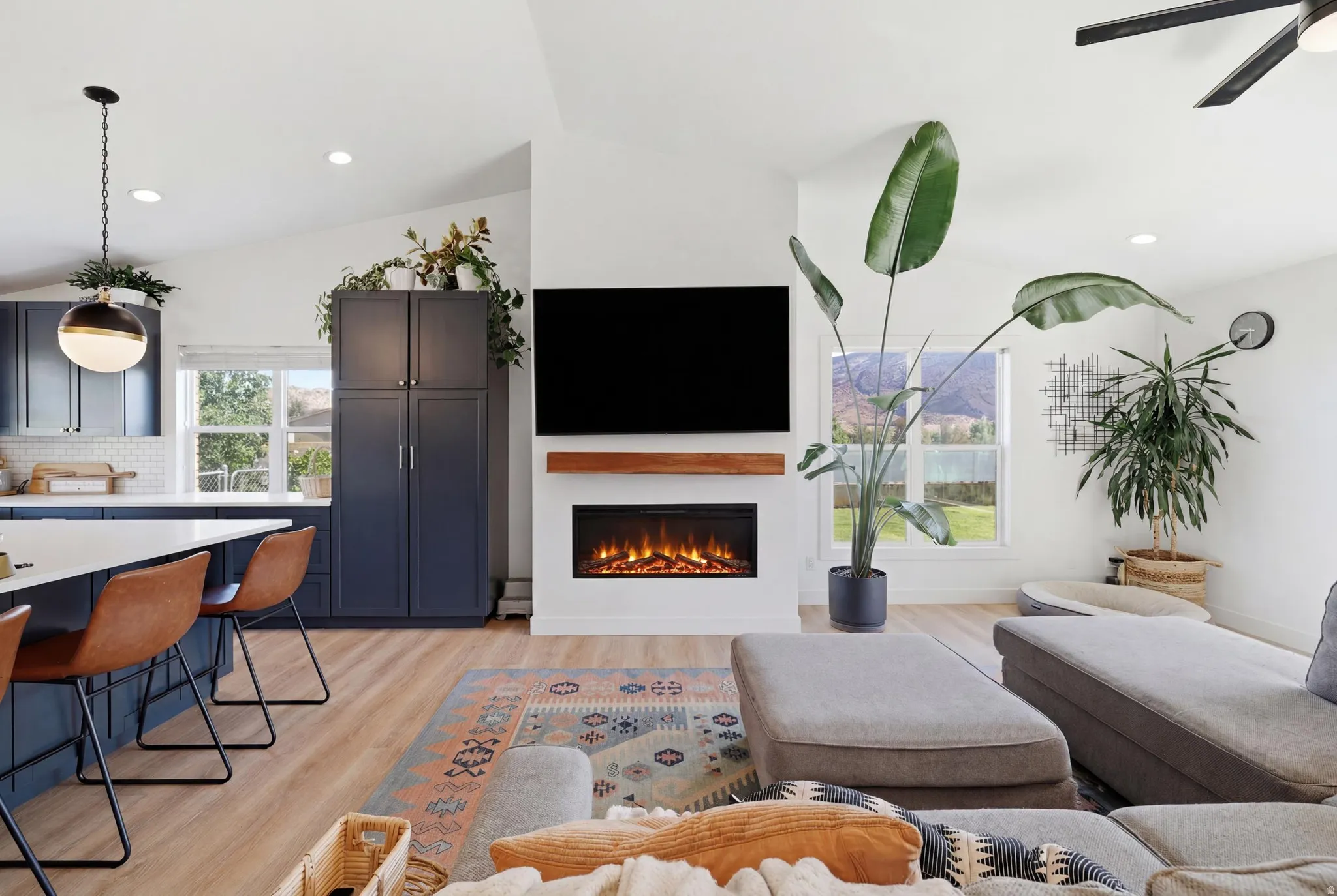 Open-concept living space featuring vaulted ceilings, wood-finish flooring, and a modern fireplace with a wood mantle
