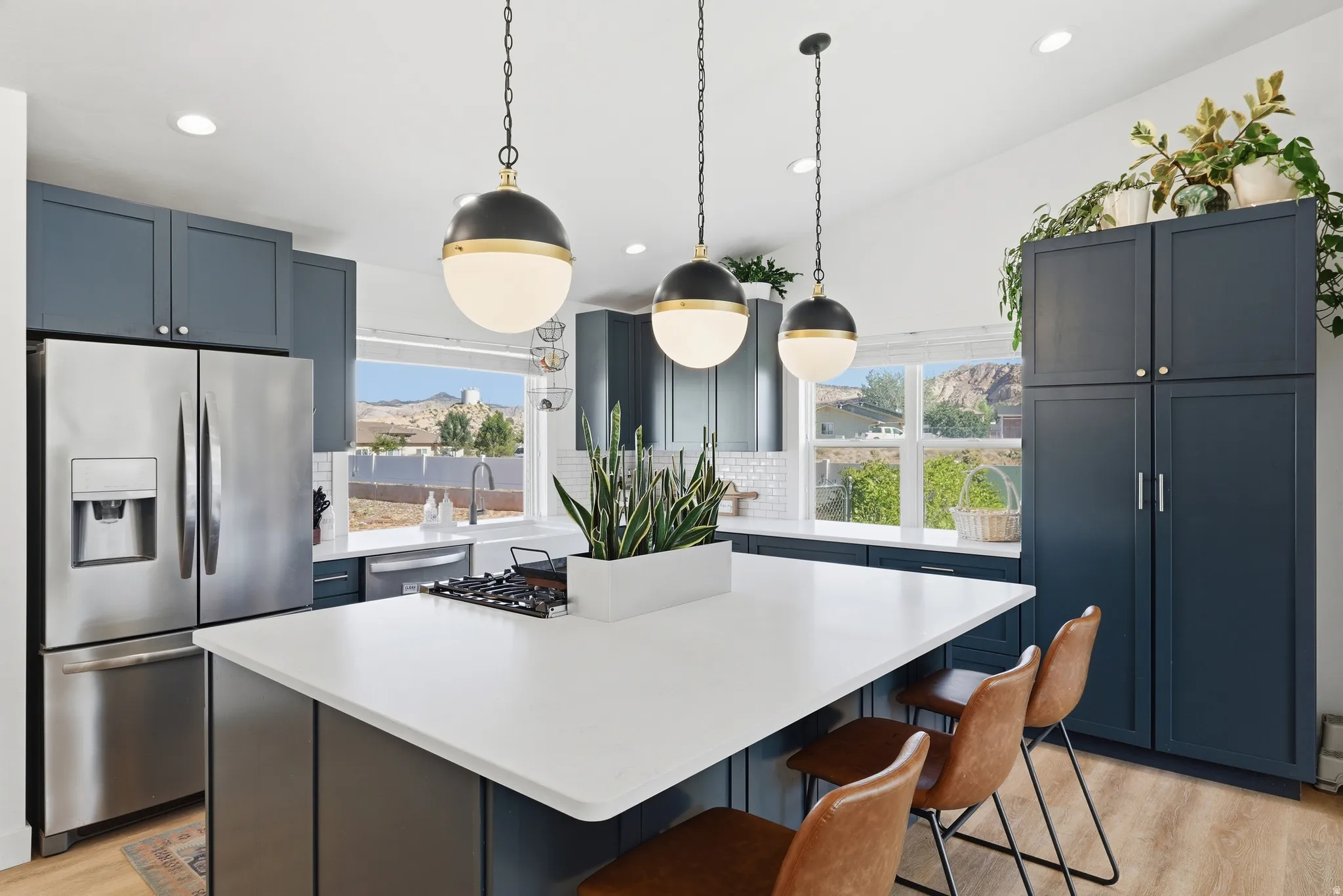 Spacious kitchen featuring an expansive central island, stainless steel appliances, dark cabinetry, white subway tile backsplash, and three pendant light fixtures