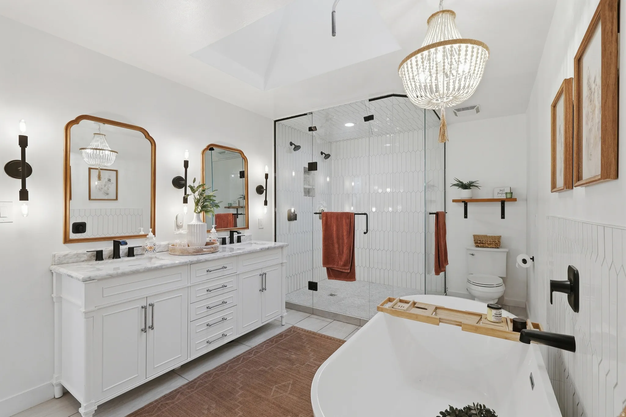 Bright bathroom featuring a double vanity with stone countertop, freestanding soaking tub, and a glass-enclosed shower with vertical tile work
