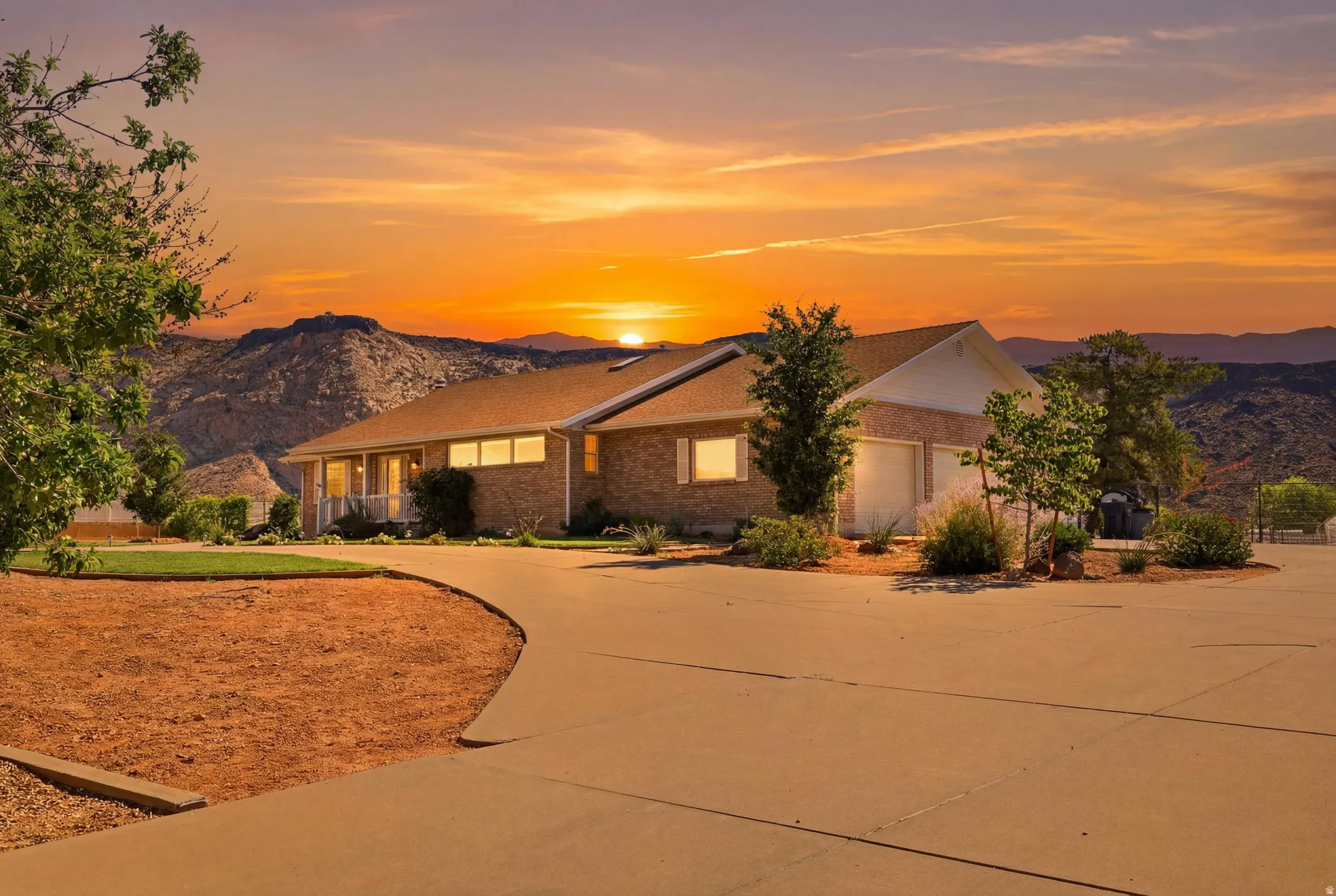 Brick exterior residence featuring a covered front porch, a two-car garage, mature landscaping, and a concrete driveway