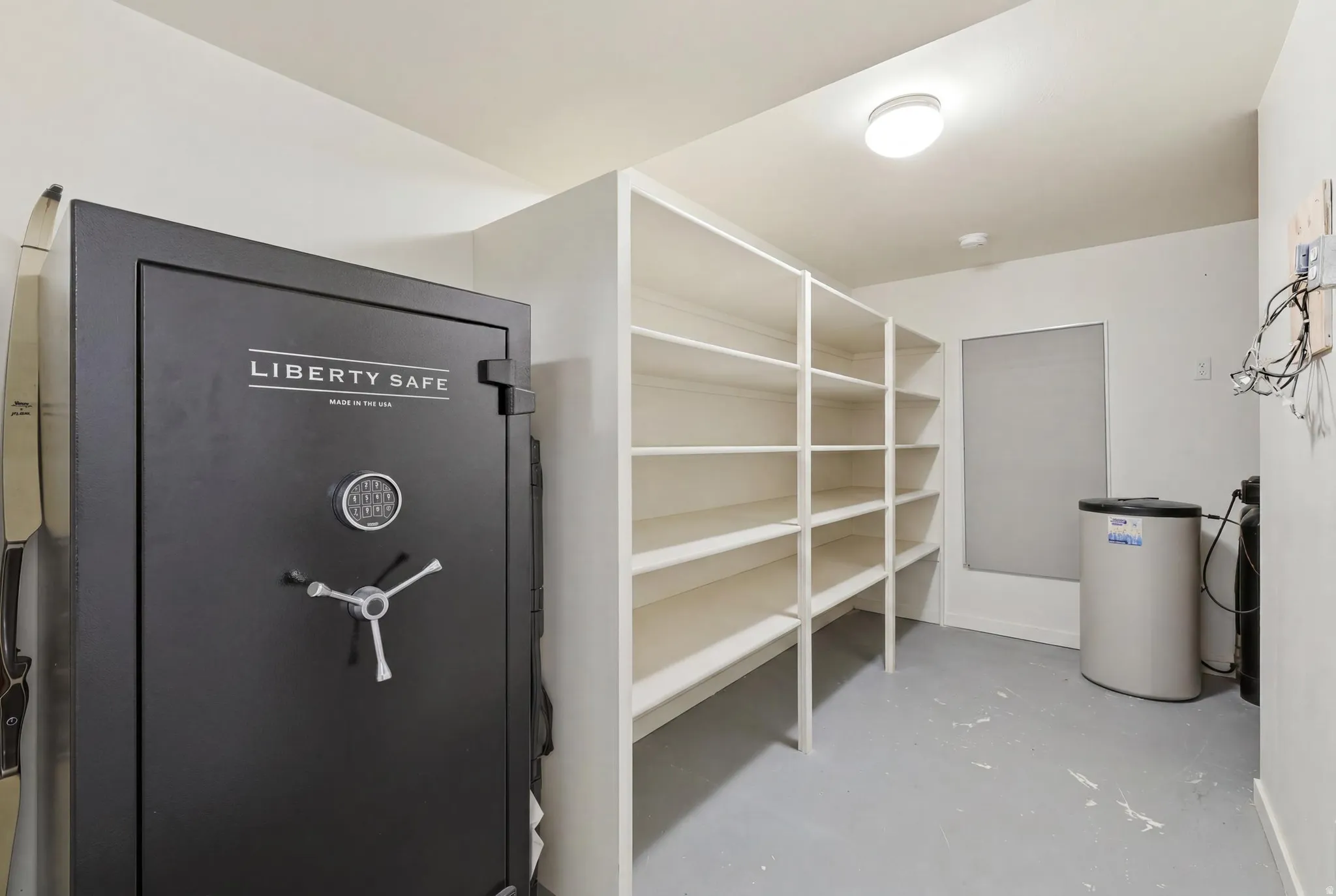 Dedicated storage room featuring a large built-in shelving system, a window with a roller shade, and an overhead flush-mount light fixture