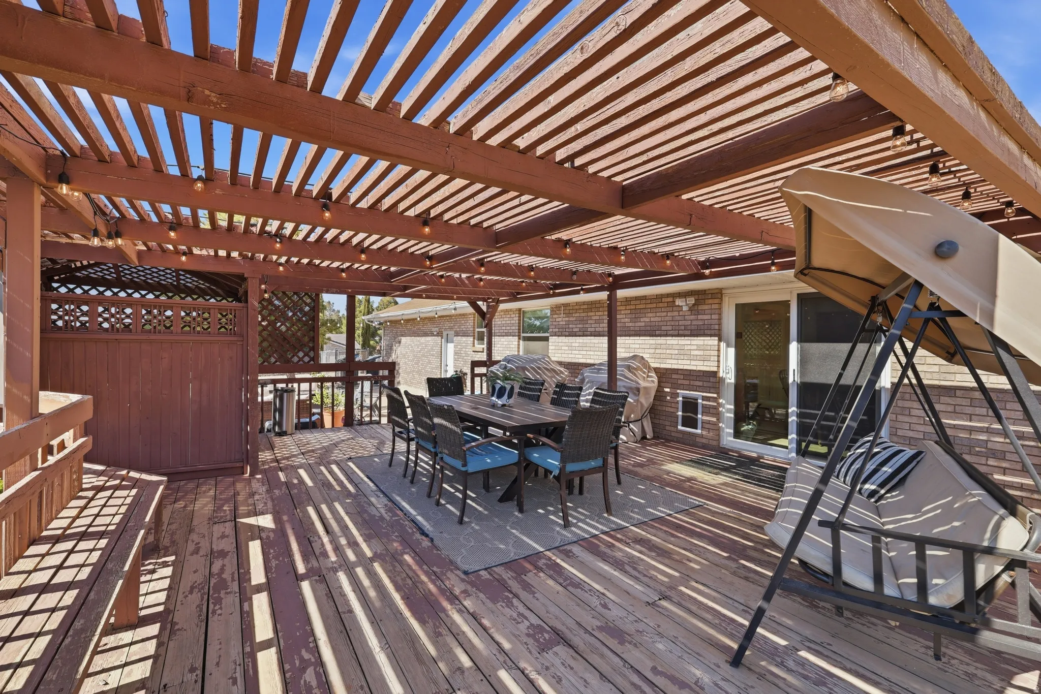 Expansive outdoor deck featuring a large wooden pergola with string lighting, a privacy screen with decorative lattice, and direct access to the interior via a sliding glass door