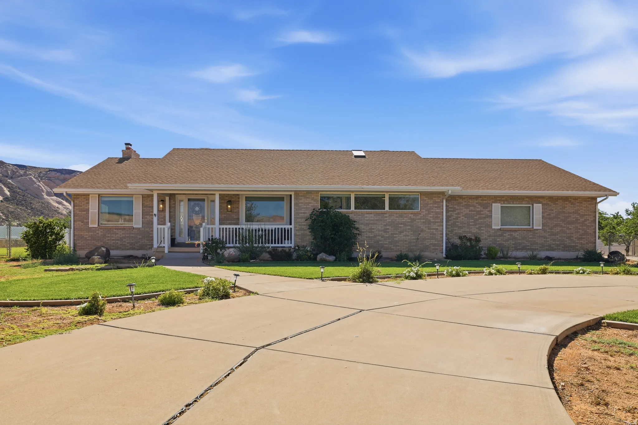 Brick exterior home featuring a covered front porch with white railing, a concrete driveway, and a shingle roof