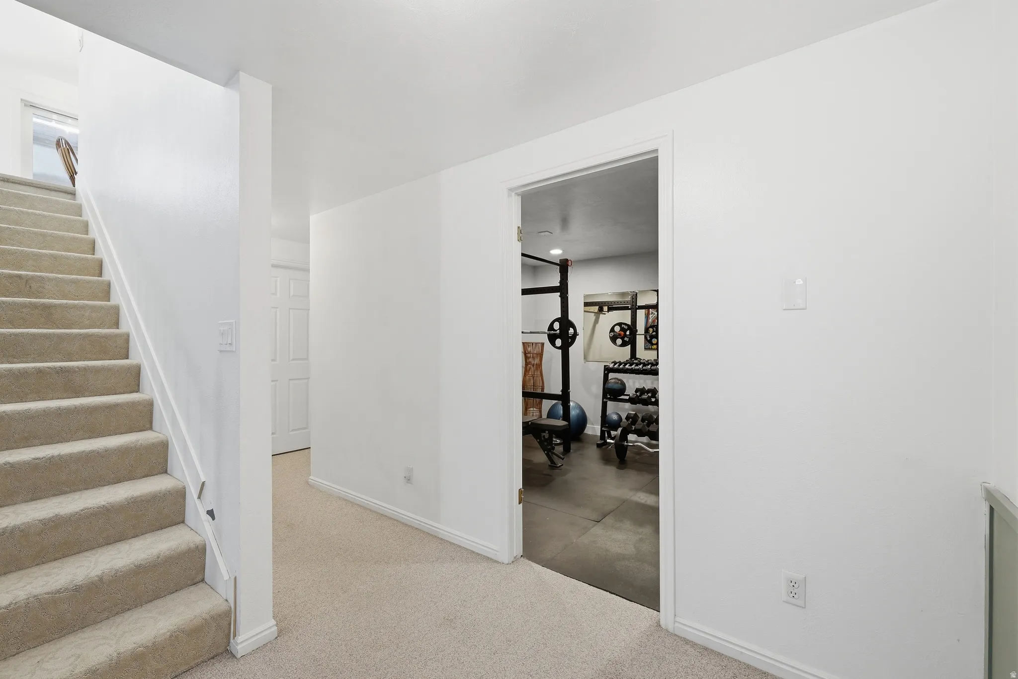 Carpeted staircase leading to an upper level with an adjacent doorway revealing a dedicated workout space