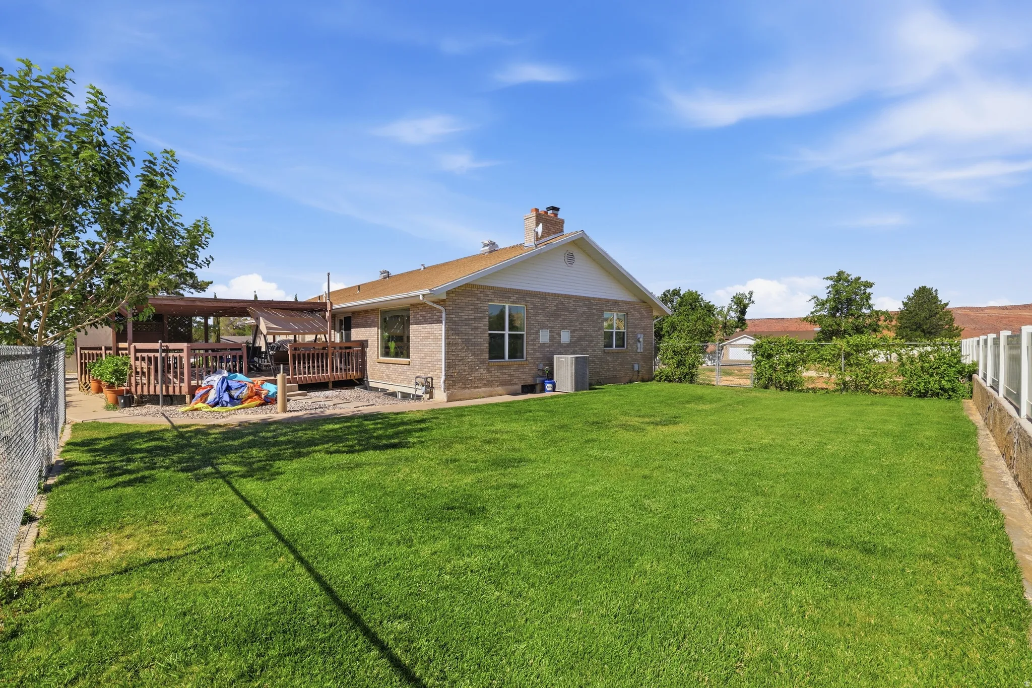 Expansive green lawn with a chain-link fence, stone retaining wall, and established plantings