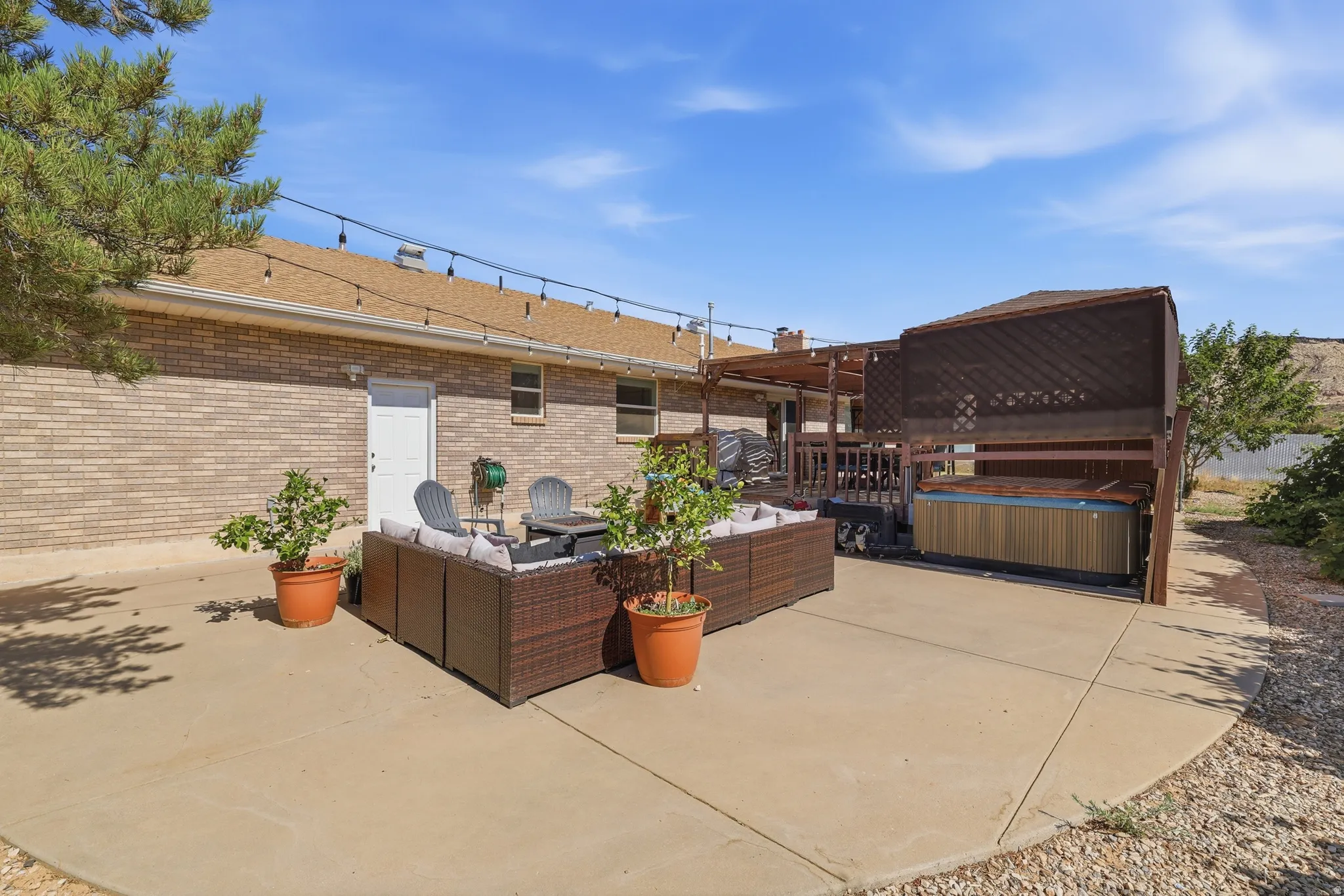 Expansive concrete patio featuring string lighting, a built-in hot tub enclosure, and a covered wooden deck structure