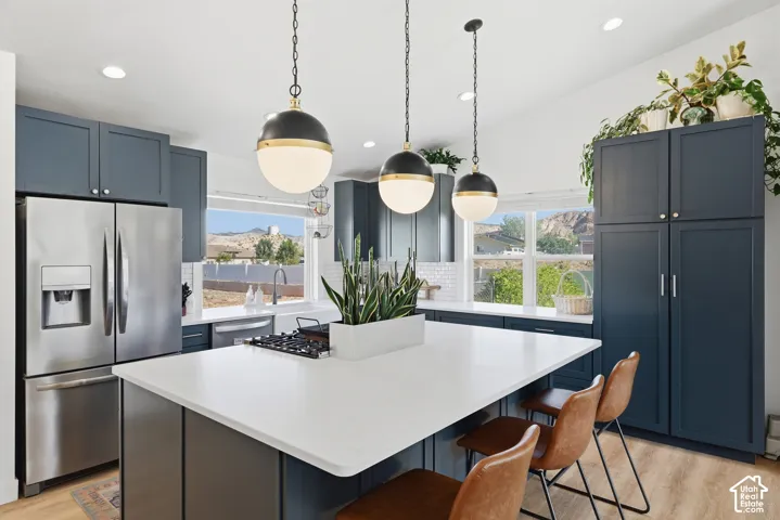 Spacious kitchen featuring an expansive central island, stainless steel appliances, dark cabinetry, white subway tile backsplash, and three pendant light fixtures