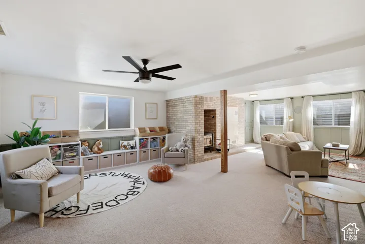 Expansive finished basement with carpet flooring, a ceiling fan, and a brick-surround fireplace