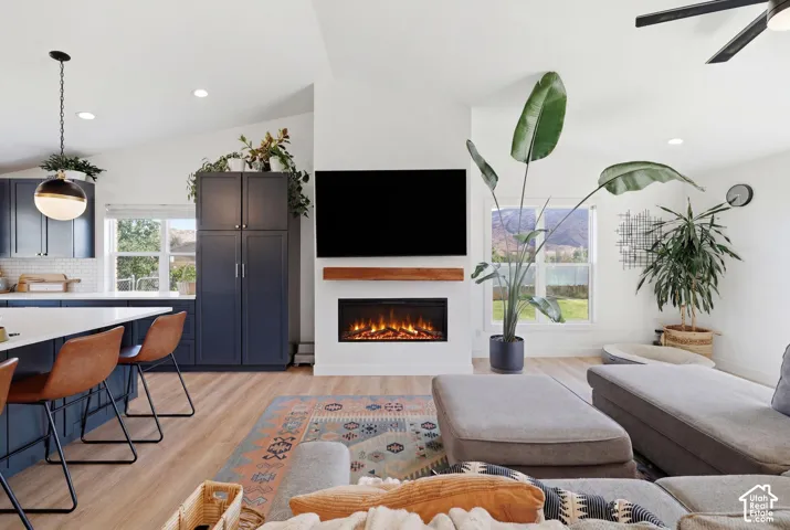 Open-concept living space featuring vaulted ceilings, wood-finish flooring, and a modern fireplace with a wood mantle