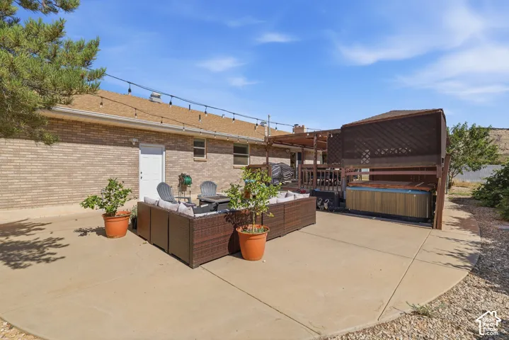 Expansive concrete patio featuring string lighting, a built-in hot tub enclosure, and a covered wooden deck structure
