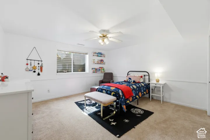 Carpeted room featuring a ceiling fan with light, a window with blinds, and white walls with wainscoting