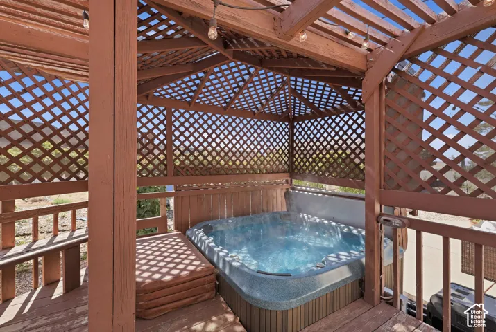 Outdoor spa enclosure featuring a lattice roof and sides, natural wood decking, and string lighting