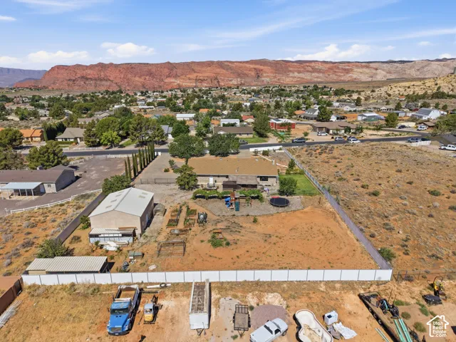Expansive property featuring a single-story residence, a large detached workshop, fenced perimeter, mature trees, and a mountain backdrop