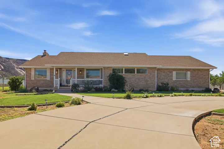 Brick exterior home featuring a covered front porch with white railing, a concrete driveway, and a shingle roof