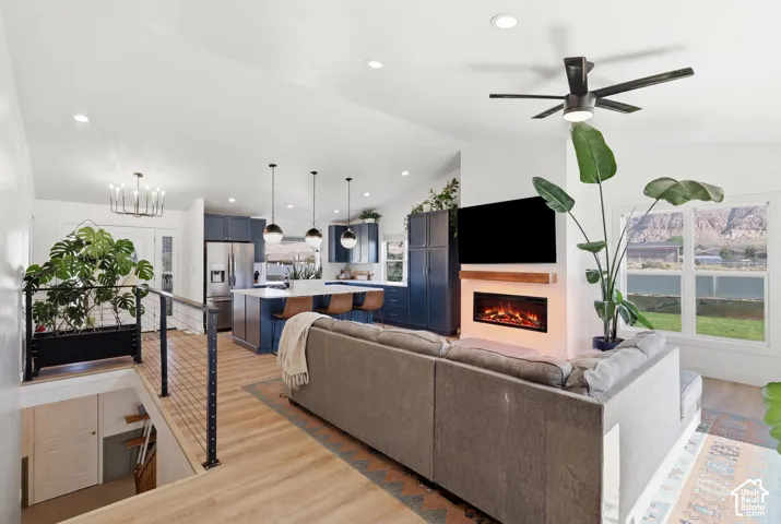 Open-concept living area featuring wood-finish flooring, a contemporary electric fireplace with a wood mantel, a modern ceiling fan, and a kitchen with navy cabinetry and a white island