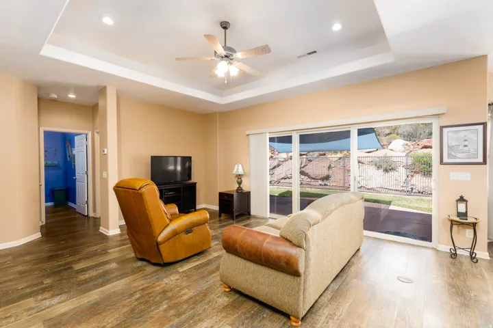 Spacious interior room featuring wood-finish flooring, a tray ceiling with recessed lighting, and a ceiling fan