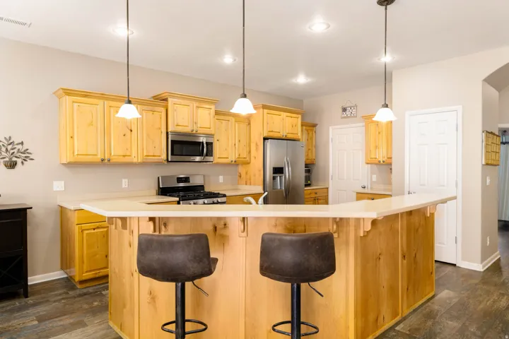 Kitchen featuring wood cabinetry, stainless steel appliances, light-toned countertops, a breakfast bar with pendant lighting, and wood-finish flooring