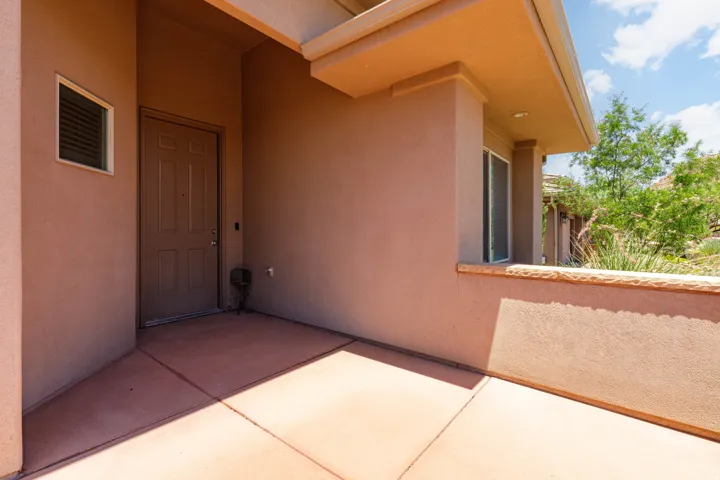 Entryway featuring a panel door with sidelight, stucco exterior, covered porch, concrete flooring, and a low privacy wall