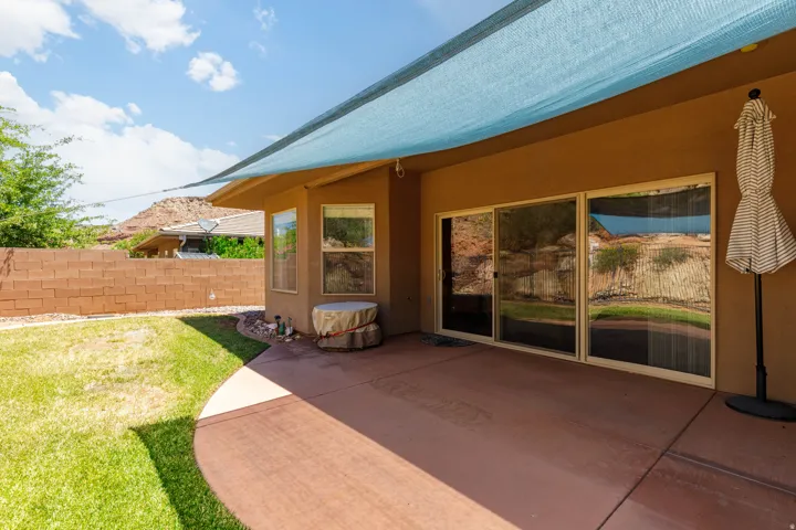 Expansive concrete patio featuring a blue shade sail and stucco exterior