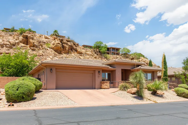 Contemporary stucco exterior with an attached garage, a paved driveway, and desert-inspired landscaping