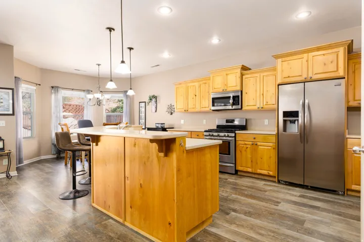 Open-concept kitchen featuring light wood cabinetry, stainless steel appliances, and a central island with bar seating