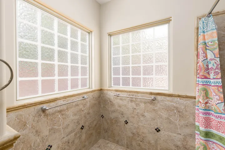 Bathroom featuring two glass block windows, a tiled shower surround with decorative square accents, and a chrome towel bar