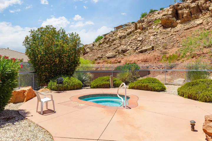 Outdoor spa with integrated steps and handrail, surrounded by a concrete patio and gravel landscaping