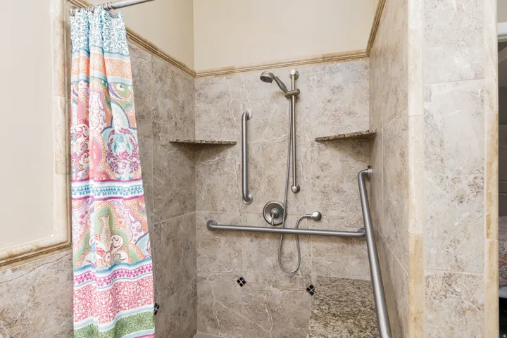 Tiled shower with handheld shower fixture, built-in seating, two corner shelves, and multiple grab bars