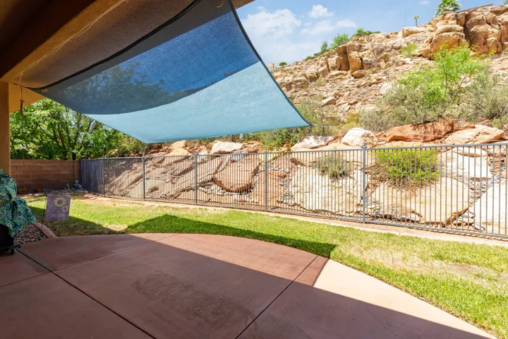 Outdoor patio with a blue shade sail, concrete paving, and a lawn area
