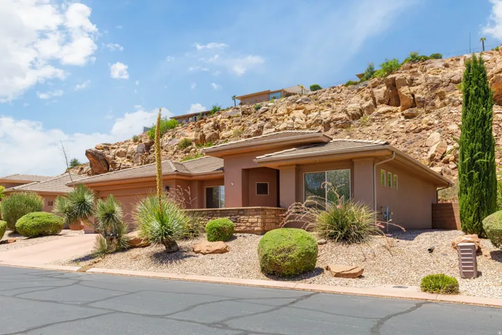 Contemporary stucco exterior with a stone accent retaining wall, xeriscaped front yard, and an integrated two-car garage