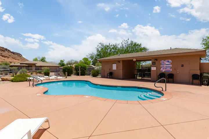 Curved swimming pool with integrated steps, surrounded by a concrete deck and a tan-stucco pool house