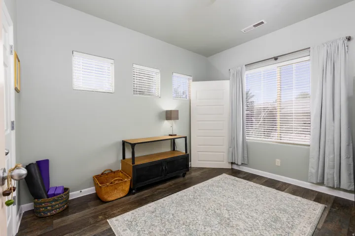 Room featuring wood-finish flooring, a large window with blinds and curtains, and three high-set rectangular windows