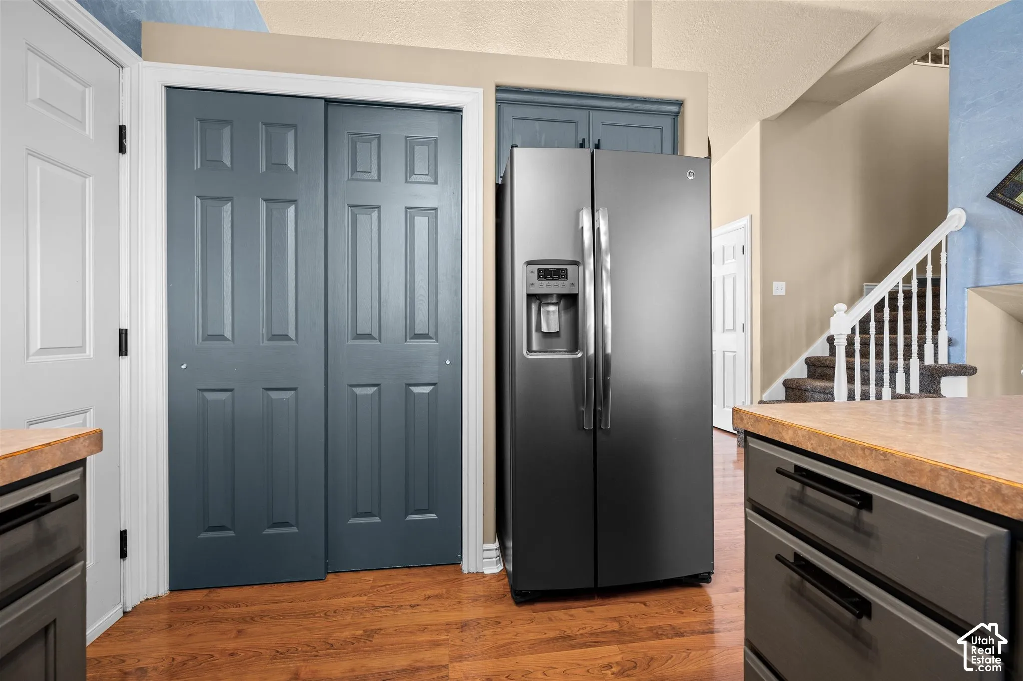 Kitchen area featuring wood-finish flooring, a stainless steel side-by-side refrigerator, and dark paneled cabinetry with black hardware