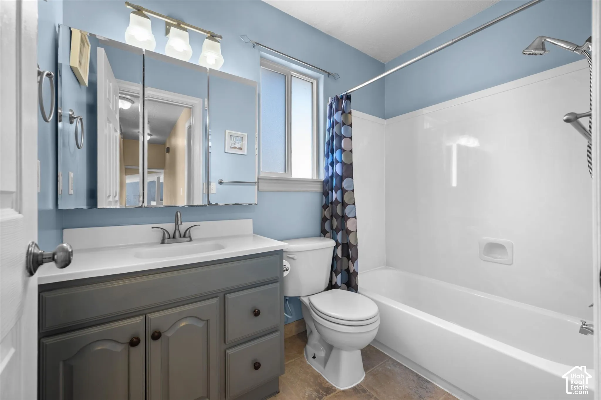 Bathroom featuring a white bathtub and shower with a wall-mounted showerhead, a single vanity with a gray cabinet and white countertop, and a mirrored medicine cabinet with integrated lighting
