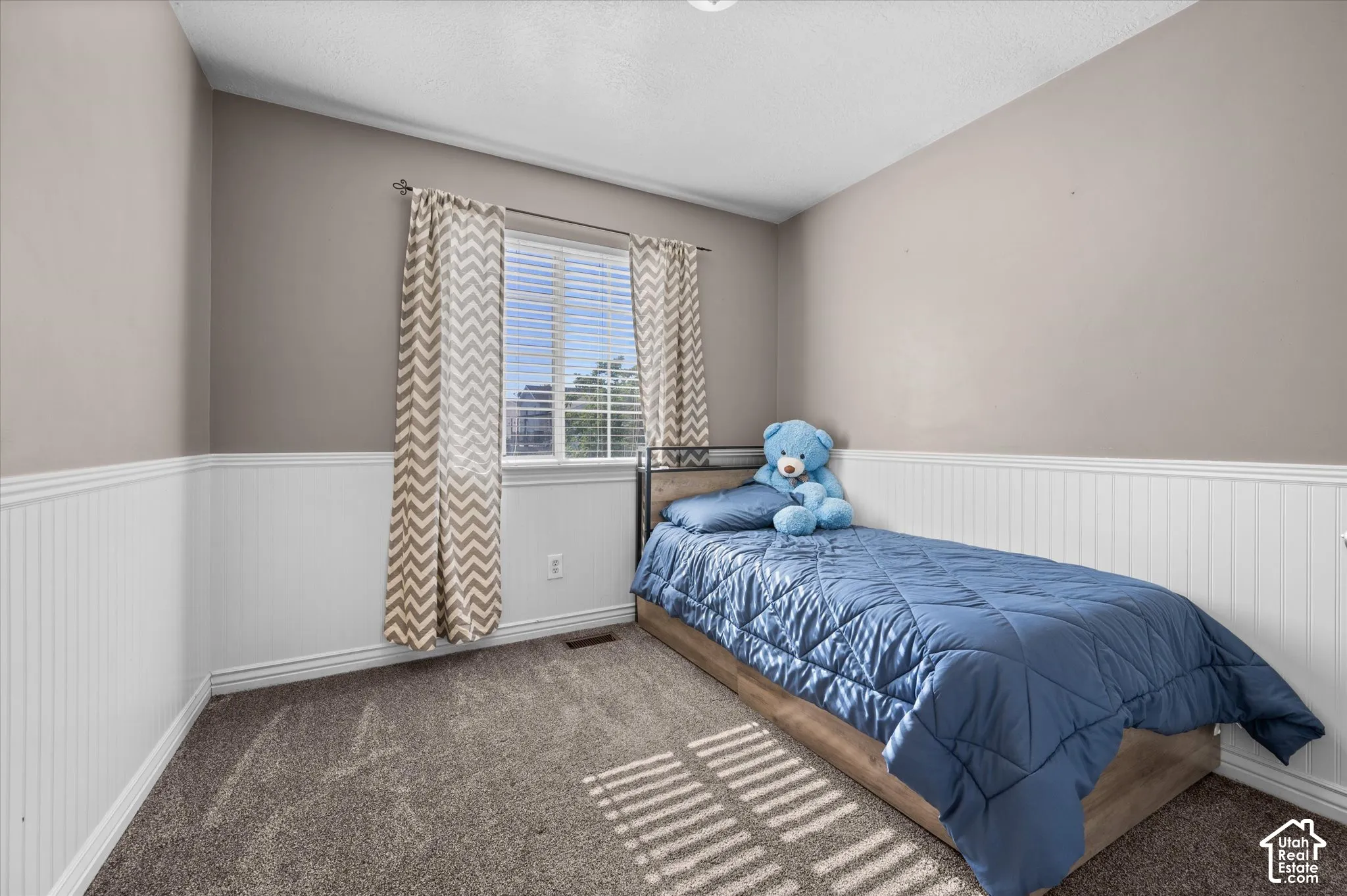 Bedroom featuring wainscoting, neutral tone walls, and a large window with blinds