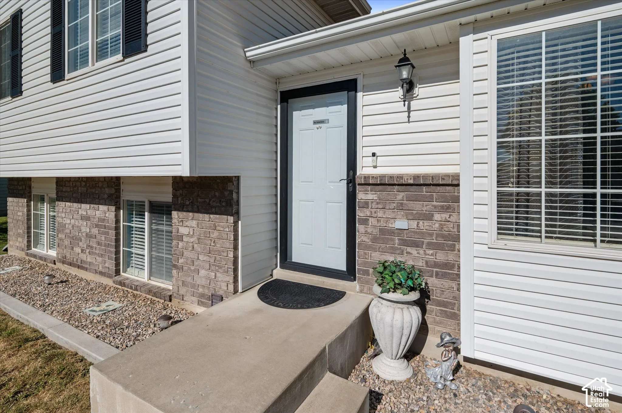 Exterior featuring white siding, brick veneer, and a white front door with a black storm door