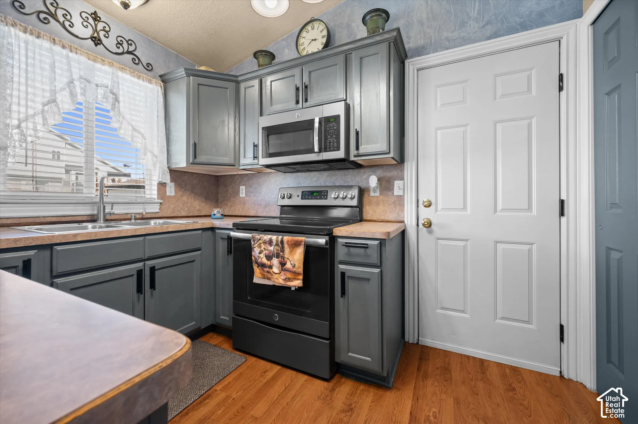 Kitchen featuring wood-finish flooring, gray cabinetry with dark hardware, stainless steel microwave, and a window above the sink