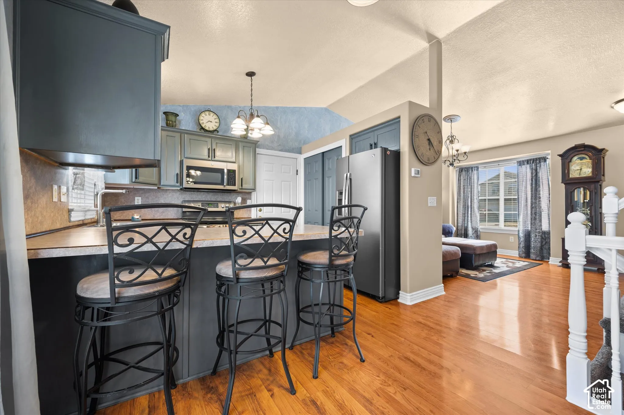 Kitchen featuring a breakfast bar with seating for three, stainless steel appliances, wood-finish flooring, and vaulted ceilings