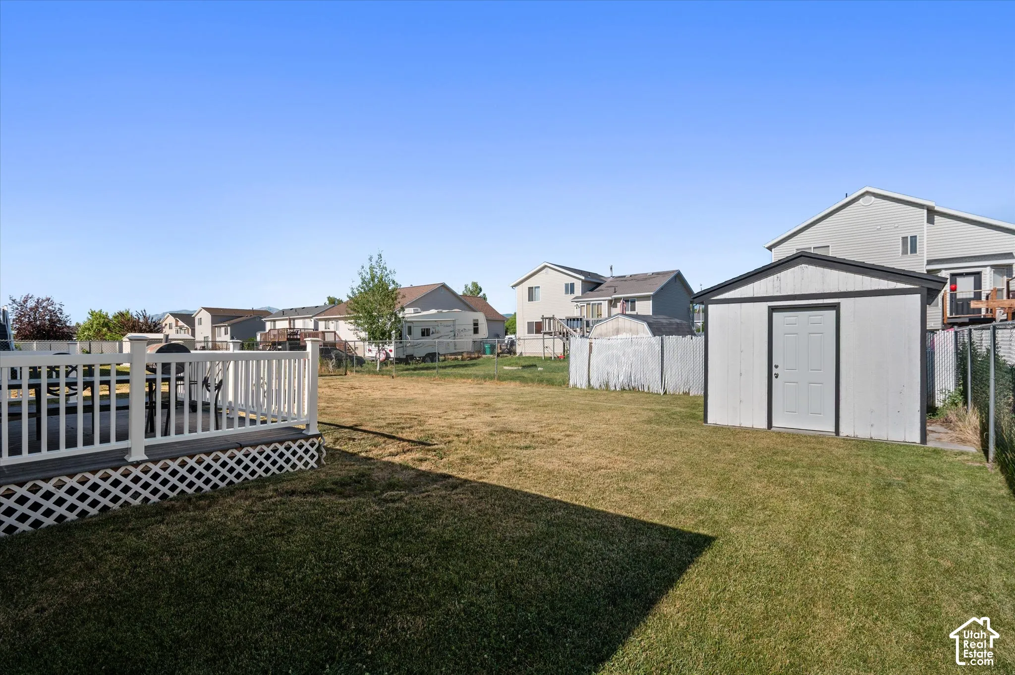 Spacious backyard featuring a white lattice-skirted deck with white railing, a separate storage shed with a light gray door, and a grass lawn