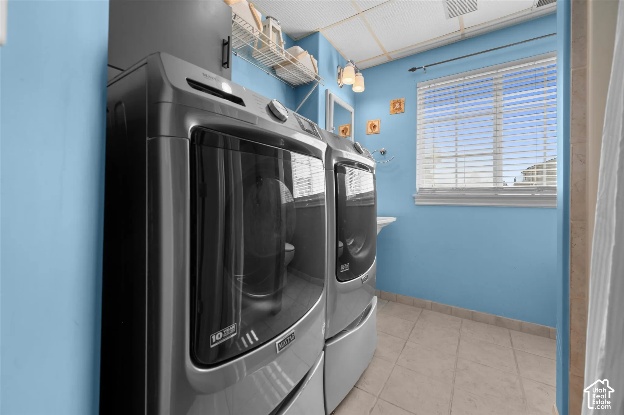 Utility space featuring ceramic tile flooring, a window with blinds, wall-mounted lighting, and a pedestal sink
