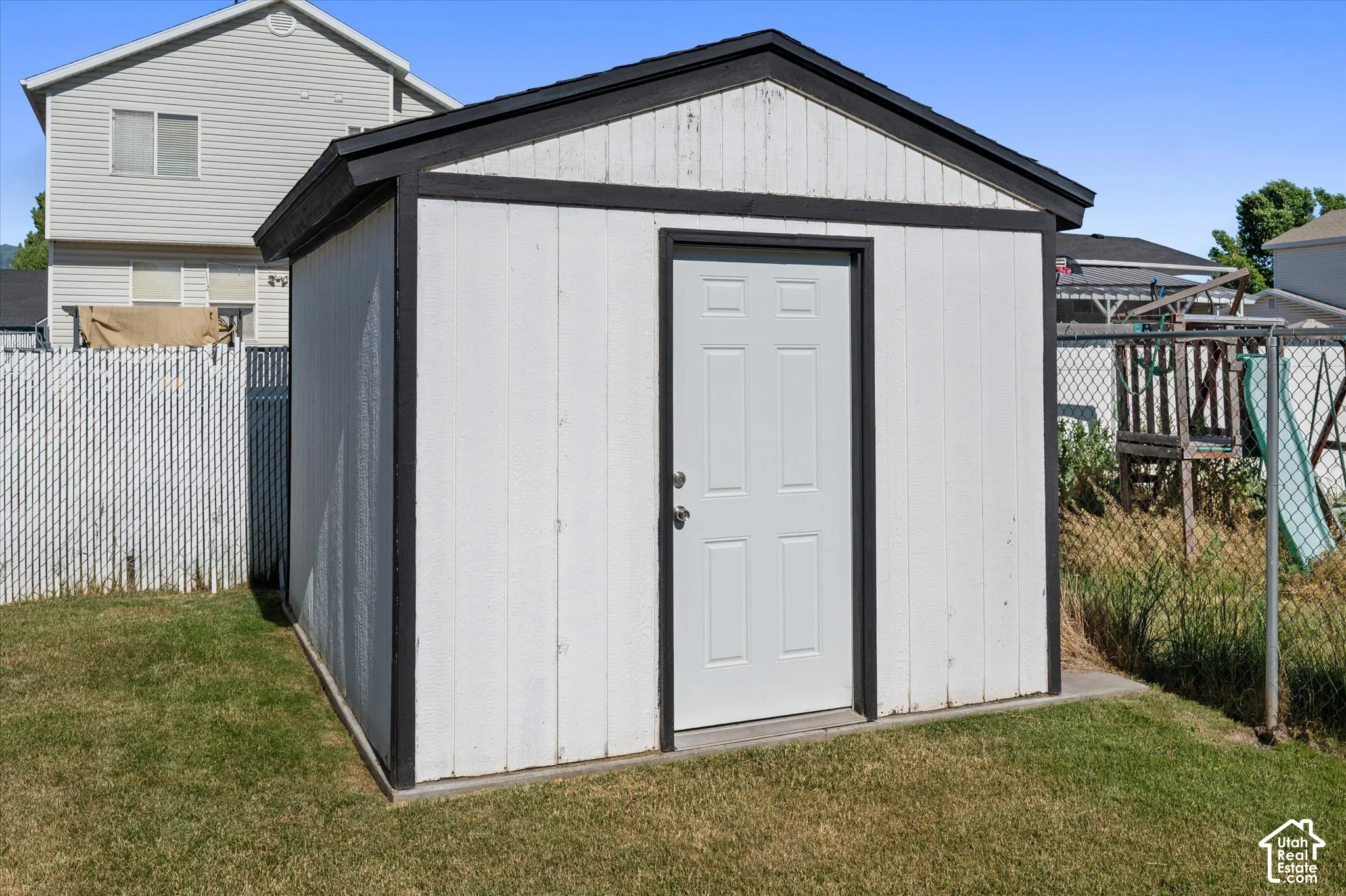 White storage shed with a contrasting black trim, featuring a single panel door with a silver knob and lock